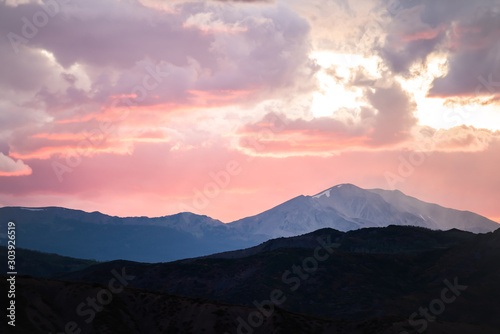 Pink purple red soft light glow sunrise in Aspen, Colorado with rocky mountains peak and vibrant color of clouds at twilight with mountain ridge silhouette