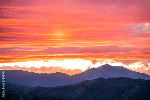 Aspen, Colorado rocky mountains vibrant vivid colorful red sunset orange yellow light in sky with clouds and mountain ridge silhouette