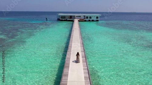 Aerial, drone shot, towards a woman cycling towards a resort, on the Conrad Rangali island, suroounded by the turquoise sea, on a sunny day, in Maldives photo