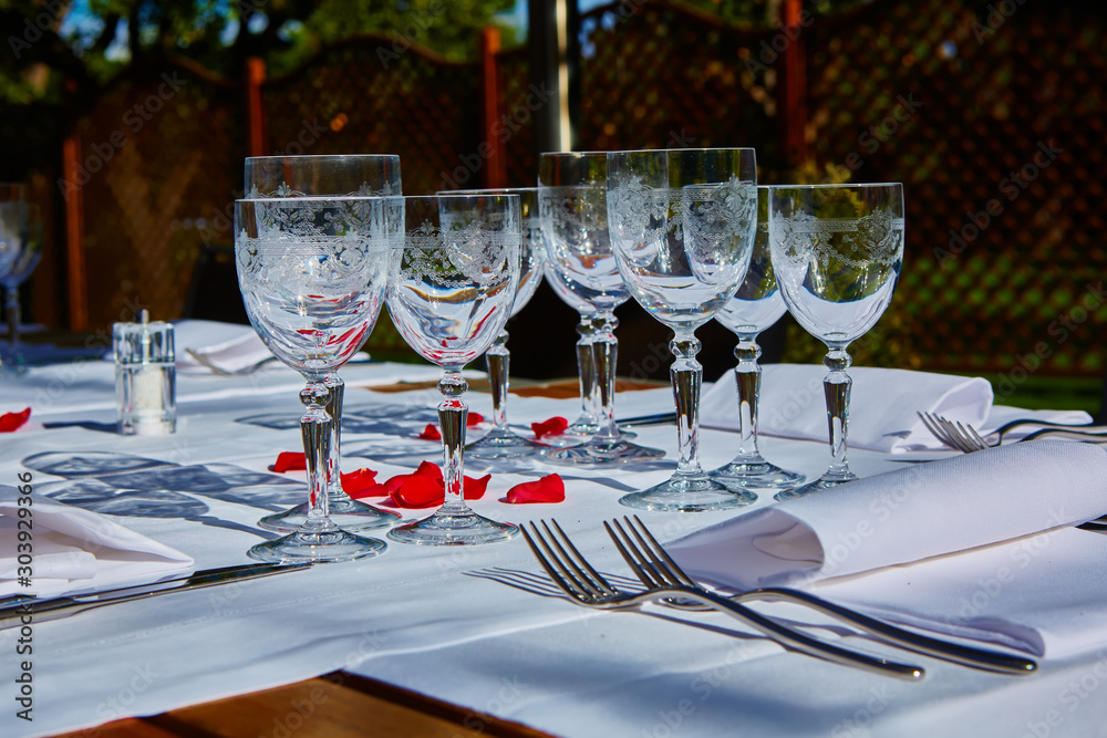 Fine dining table setting with white china and wine and water crystal glasses, with silverware in the order of use, and romantic red tablecloth ready for guests at an event, wedding or at a restaurant Fine dining table setting with white china and wine and water crystal glasses, with silverware in the order of use, and romantic red tablecloth ready for guests at an event, wedding or at a restaurant