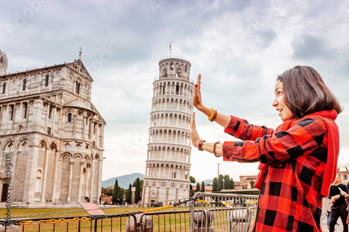 Funny Asian girl supporting famous leaning tower in Pisa. Travel concept photo