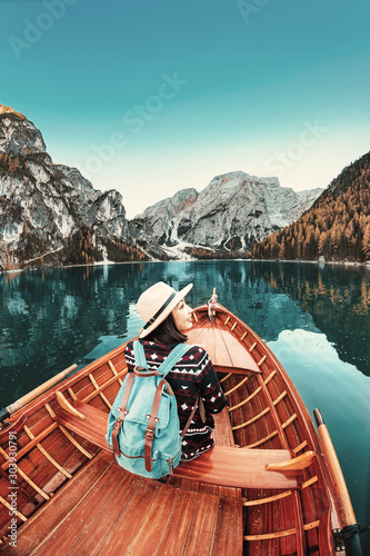 Happy asian traveler girl with backpack sitting in vintage wooden boat at the Braies lake in Dolomites Alps, Italy