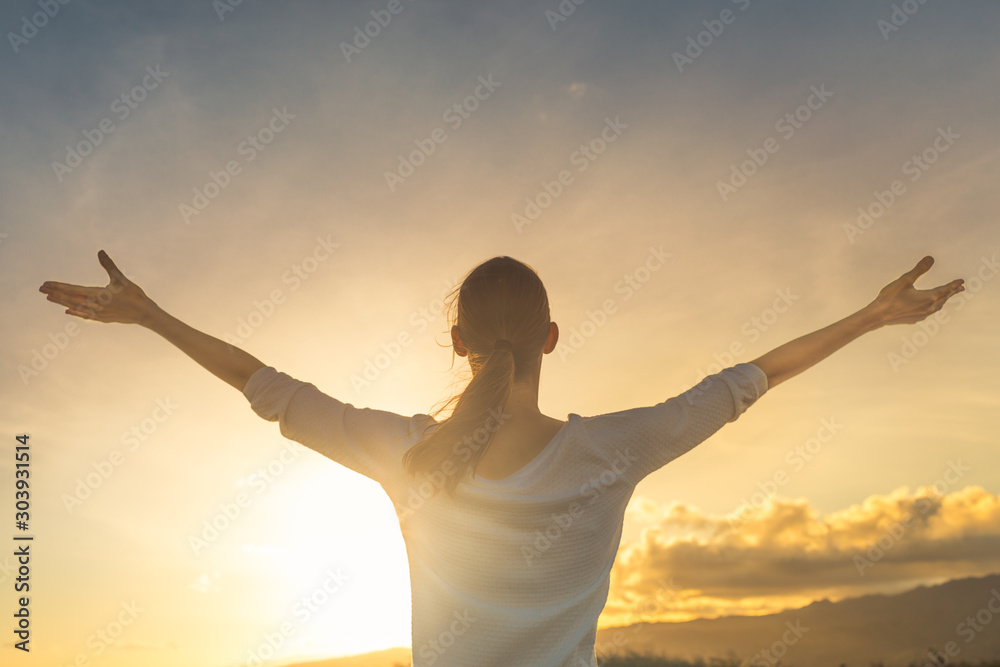 Happy young woman feeling free putting arms up to the sunset sky feeling good. 