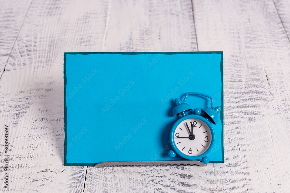 Mini blue alarm clock stand tilted above buffer wire in front of notepaper Mini blue alarm clock stand tilted above buffer wire in front of notepaper