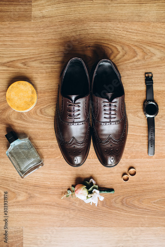 Men's accessories, perfume, boutonniere, gold rings, watches and leather shoes of the groom on a wooden table. Businessman clothing detail concept. Luxury men's accessories. Stylish men's shoes.