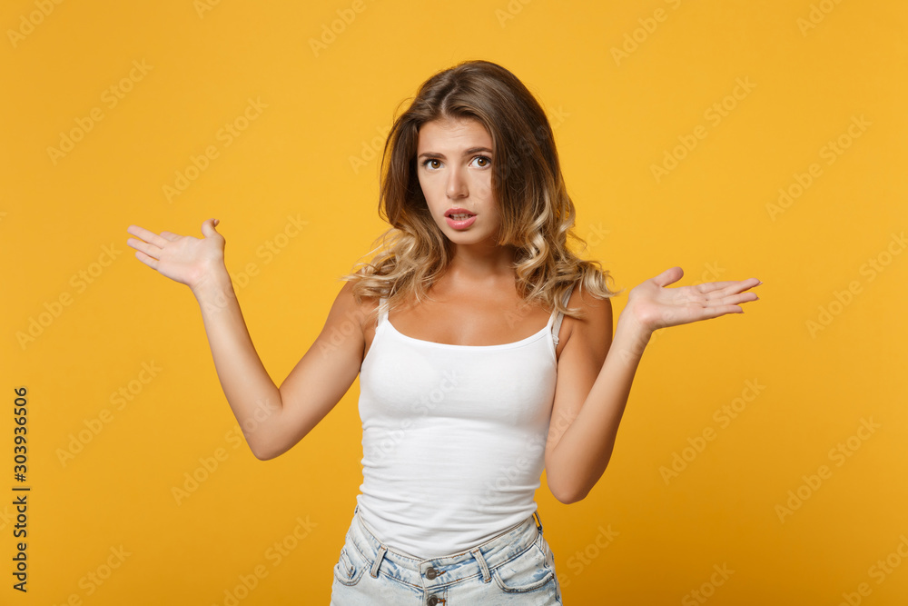 Confused young woman girl in light casual clothes posing isolated on yellow orange background in studio. People sincere emotions lifestyle concept. Mock up copy space. Pointing spreading hands aside.