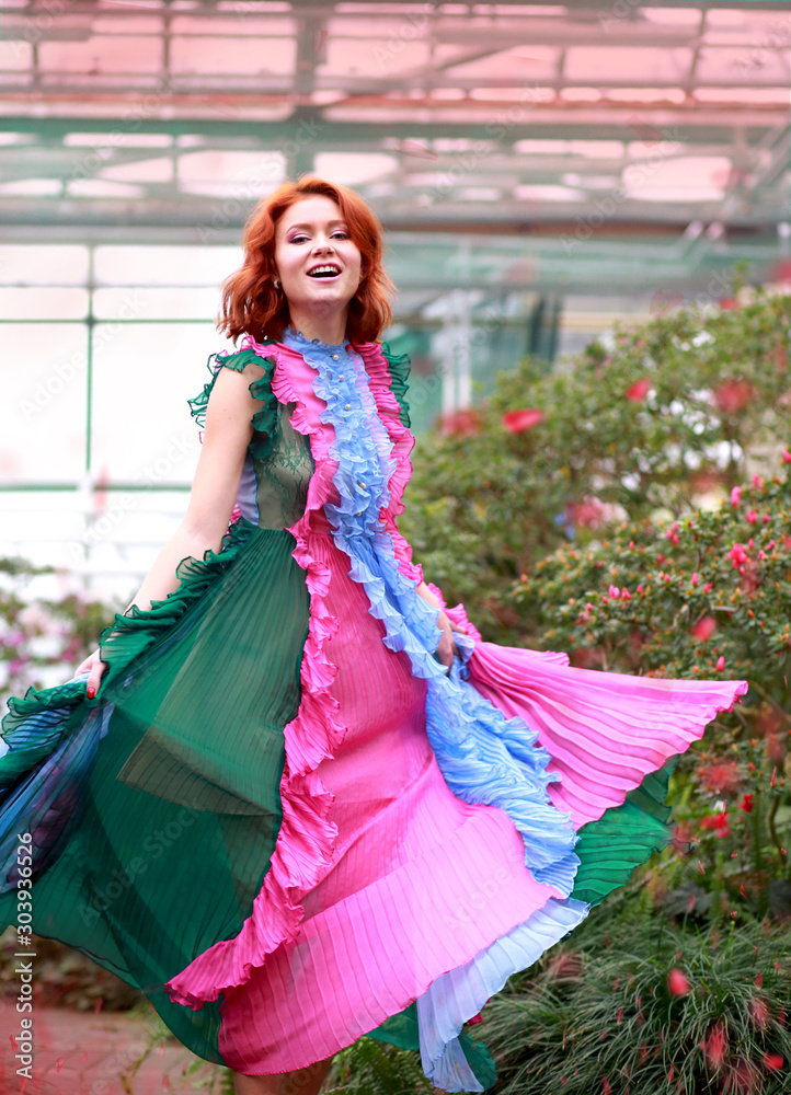 Fototapeta premium beautiful red-haired girl in arranger where azalea blooms in a colorful flying dress
