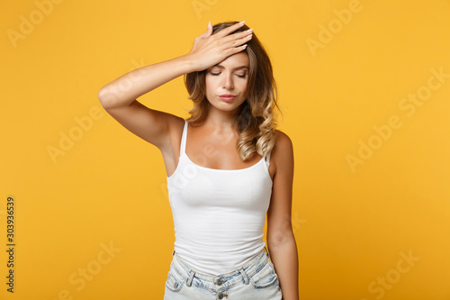 Tired young woman in light casual clothes posing isolated on yellow orange background, studio portrait. People sincere emotions lifestyle concept. Mock up copy space. Put hand on head, looking down.