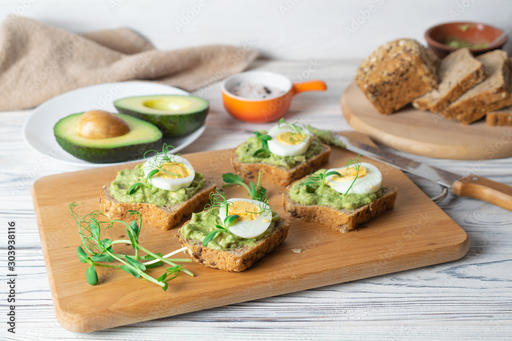 Healthy toasts with whole grain bread, avocado and boiled egg on wooden board Healthy toasts with whole grain bread, avocado and boiled egg on wooden board