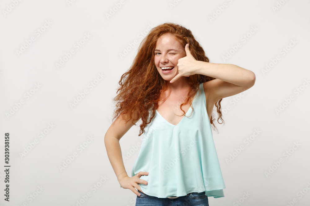 Young smiling redhead woman in casual light clothes posing isolated on white background in studio. People lifestyle concept. Mock up copy space. Doing phone gesture like says call me back, blinking.