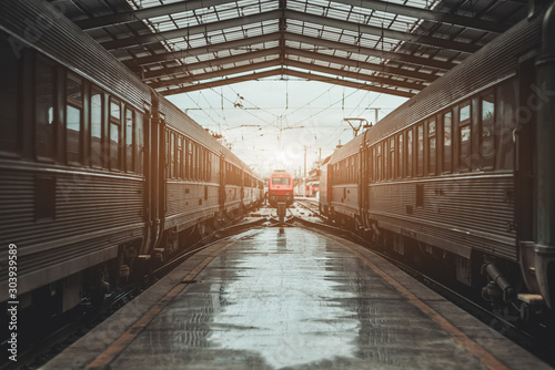Fototapeta Naklejka Na Ścianę i Meble -  Symmetrical view of a railroad station depot with a triangle roof above, a modern red locomotive being in a defocused background on maintenance, two high-speed trains on both sides of the platform