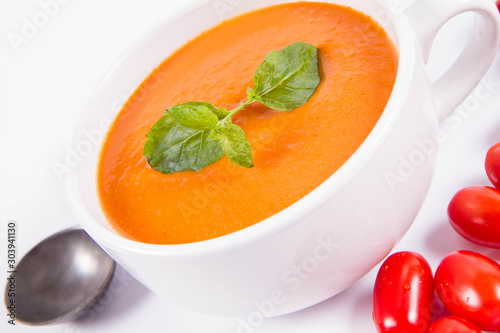 Gazpacho soup decorated with fresh mint and some tomatoes on a white background with a vintage spoon
