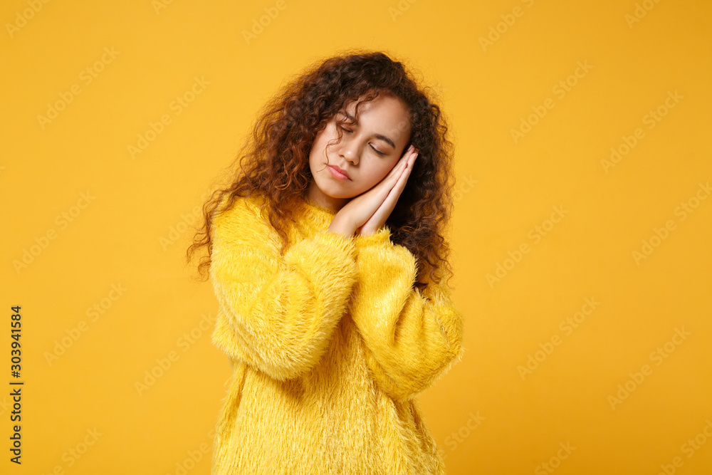 Relaxed young african american girl in fur sweater posing isolated on yellow orange wall background, studio portrait. People lifestyle concept. Mock up copy space. Sleep with folded hands under cheek. Relaxed young african american girl in fur sweater posing isolated on yellow orange wall background, studio portrait. People lifestyle concept. Mock up copy space. Sleep with folded hands under cheek.