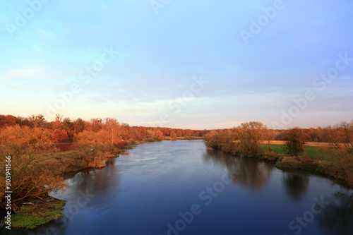 Fototapeta Naklejka Na Ścianę i Meble -  Brązowe i czerwone drzewa nad rzeką w świetle zachodzącego słońca.