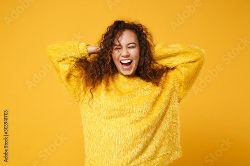 Laughing young african american girl in fur sweater posing isolated on yellow orange background studio portrait. People lifestyle concept. Mock up copy space. Put hands on head, keeping eyes closed. © ViDi Studio