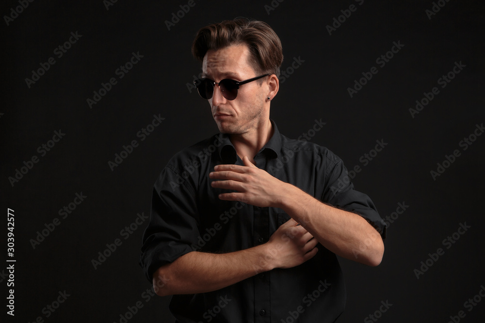 Confident stylish bussinesman in black eyeglasses buttoning up balck shirt isolated over black background. Confident stylish bussinesman in black eyeglasses buttoning up balck shirt isolated over black background.