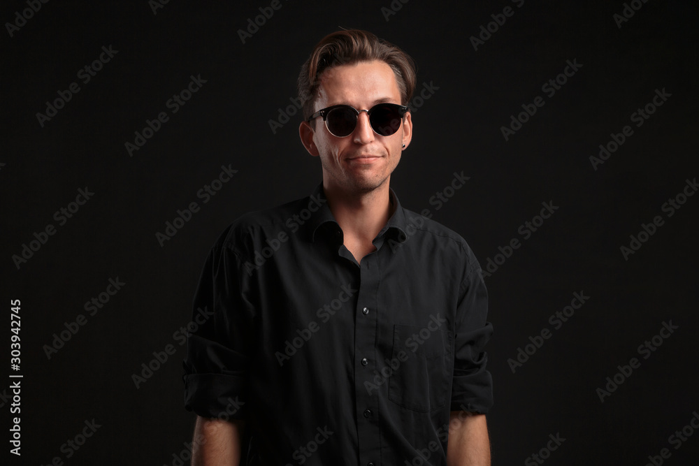 Stylish handsome man a black shirt and sun glasses isolated over black background. Low key portrait. Stylish handsome man a black shirt and sun glasses isolated over black background. Low key portrait.