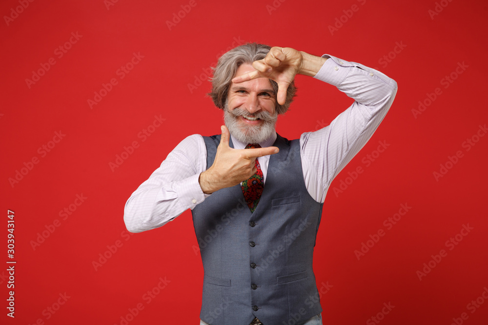 Funny elderly gray-haired mustache bearded man in classic shirt vest colorful tie isolated on red background in studio. People lifestyle concept. Mock up copy space. Making hands photo frame gesture. Funny elderly gray-haired mustache bearded man in classic shirt vest colorful tie isolated on red background in studio. People lifestyle concept. Mock up copy space. Making hands photo frame gesture.