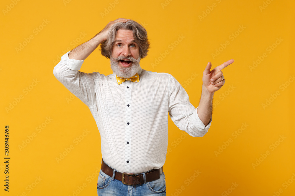 Excited elderly gray-haired mustache bearded man in white shirt bow tie posing isolated on yellow background. People lifestyle concept. Mock up copy space. Pointing finger aside, putting hand on head. Excited elderly gray-haired mustache bearded man in white shirt bow tie posing isolated on yellow background. People lifestyle concept. Mock up copy space. Pointing finger aside, putting hand on head.
