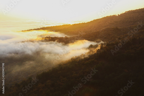Fog covers the mountains during the golden hour. The dynamic movement of fog in the mountains during sunset