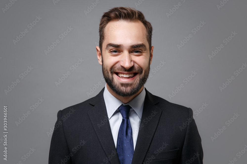 Cheerful young bearded business man in classic black suit shirt tie posing isolated on grey background studio portrait. Achievement career wealth business concept. Mock up copy space. Looking camera. Cheerful young bearded business man in classic black suit shirt tie posing isolated on grey background studio portrait. Achievement career wealth business concept. Mock up copy space. Looking camera.