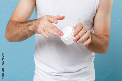 Close up cropped shot of man hand applying moisturizer cream from container isolated on blue pastel background studio portrait. Skin care healthcare cosmetic procedures concept Mock up copy space.