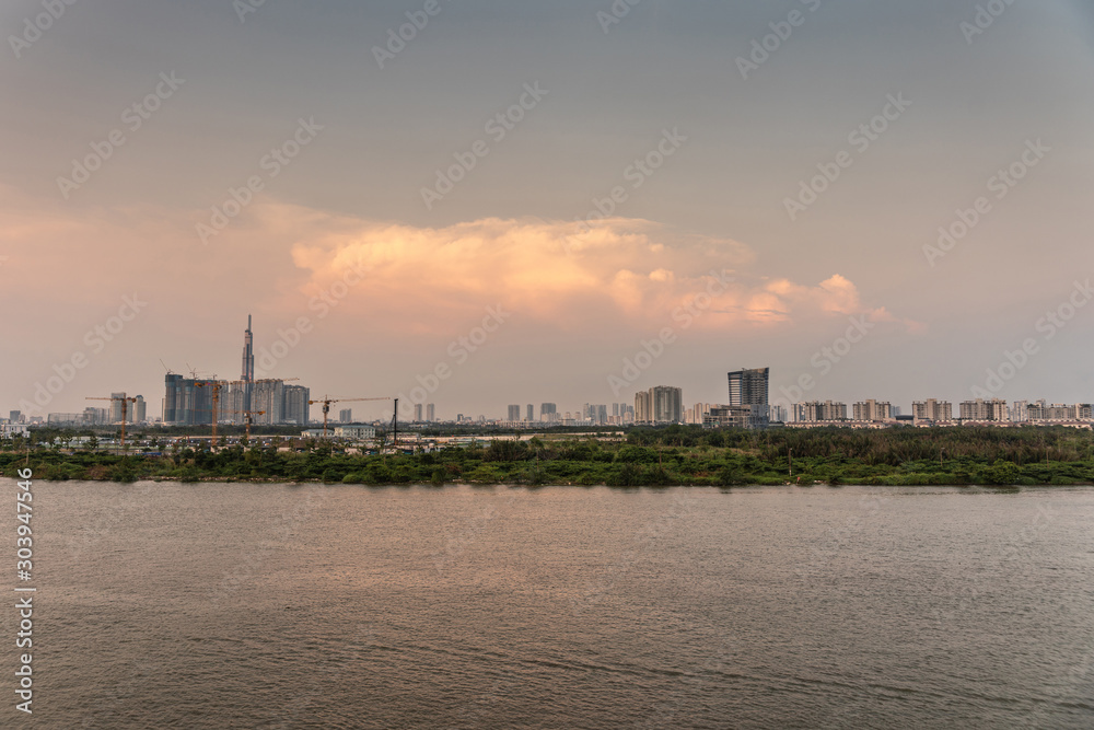Ho Chi Minh City, Vietnam - March 12, 2019: Evening shot over Song Sai Gon river towards modern part of city with high rises peeking above green belt and shorter houses. Landmark 81 tower on horizon.