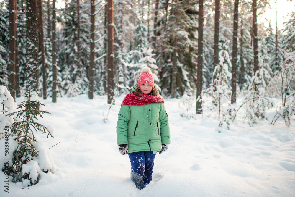 Portrait of plump funny girl in winter clothes posing for camera in snowy forest.