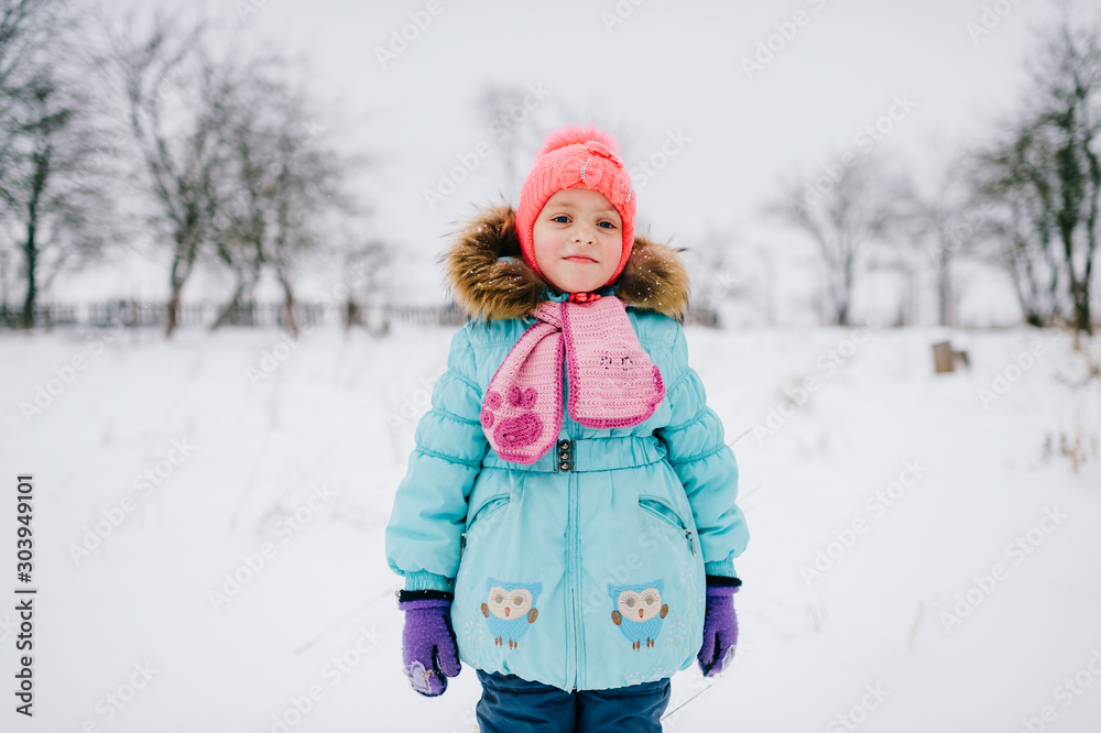 Positive little girl looking standing in snowy field and looking at camera Positive little girl looking standing in snowy field and looking at camera