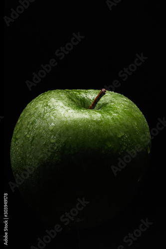 Appetizing green apple covered with drops of water on a black background. Close-up