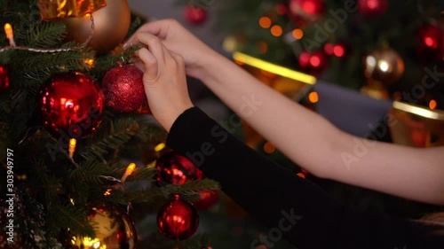 Young woman decorate a christmas tree with toys. Gold presents. Domestic festive decor