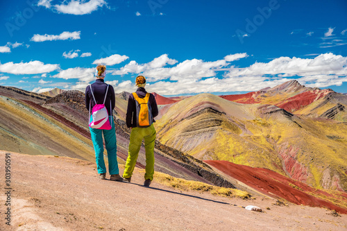 Girls watching stunning view at Palccoyo rainbow mountain (Vinicunca alternative), mineral colorful stripes in Andean valley, Cusco, Peru, South America