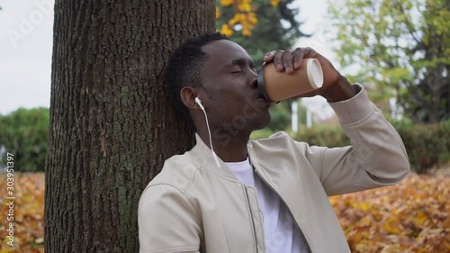 Man listens to music and takes tea in the park in autumn.