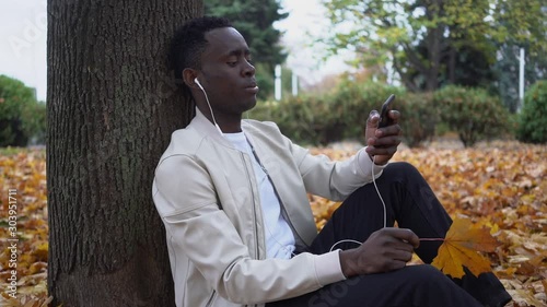 Man listens to music and takes tea in the park in autumn.