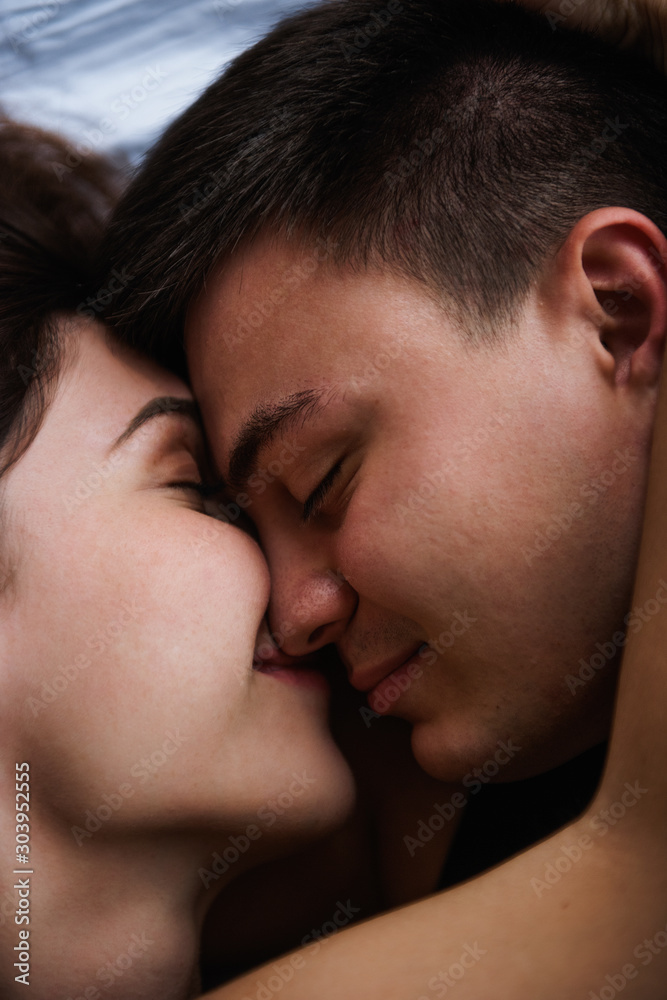 Top view of couple in love. Close-up portrait of the Lovers who lie on the bed at home, head to head. The morning of the newlyweds, tenderly resting on festive day off at home. Concept of tactility Top view of couple in love. Close-up portrait of the Lovers who lie on the bed at home, head to head. The morning of the newlyweds, tenderly resting on festive day off at home. Concept of tactility