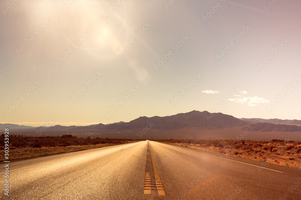 Desolate desert road with mountains with sunflare; western United Stated - obrazy, fototapety, plakaty 