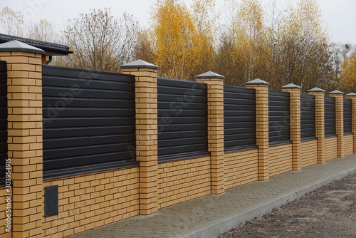 long private fence of brown planks and bricks on a rural street