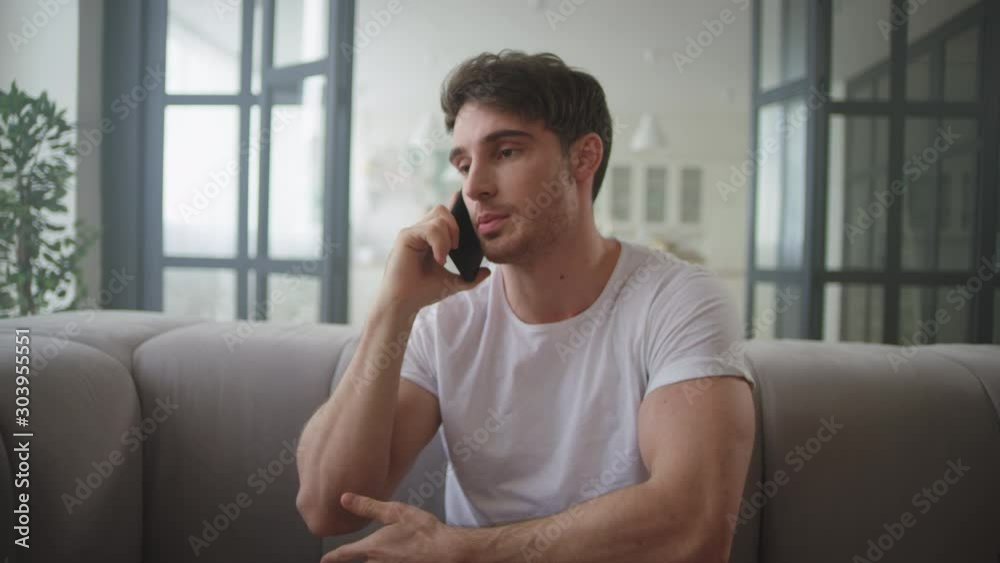 Serious businessman talking mobile phone at home. Young couple hugging on sofa. Serious businessman talking mobile phone at home. Young couple hugging on sofa.