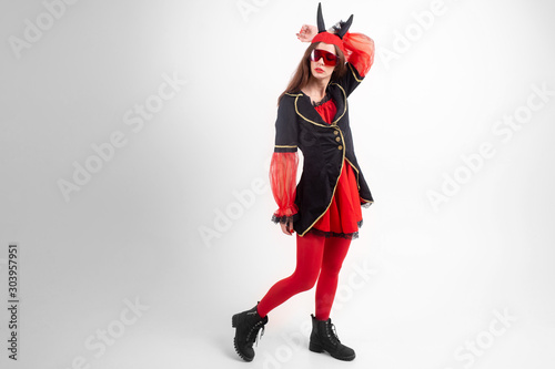 Sexy brunette girl in red tights, masquerade costume, futuristic glasses and devil horns on her head posing with passion over white background