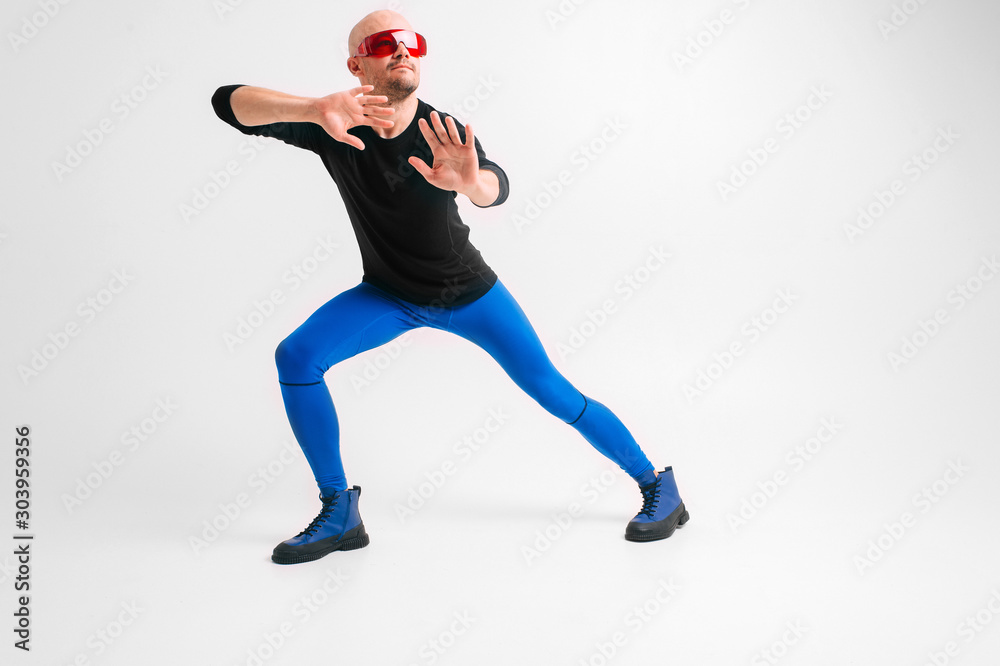 Fashion portrait of stylish man in blue tights and indigo boots stretching and exercising over white studio background.