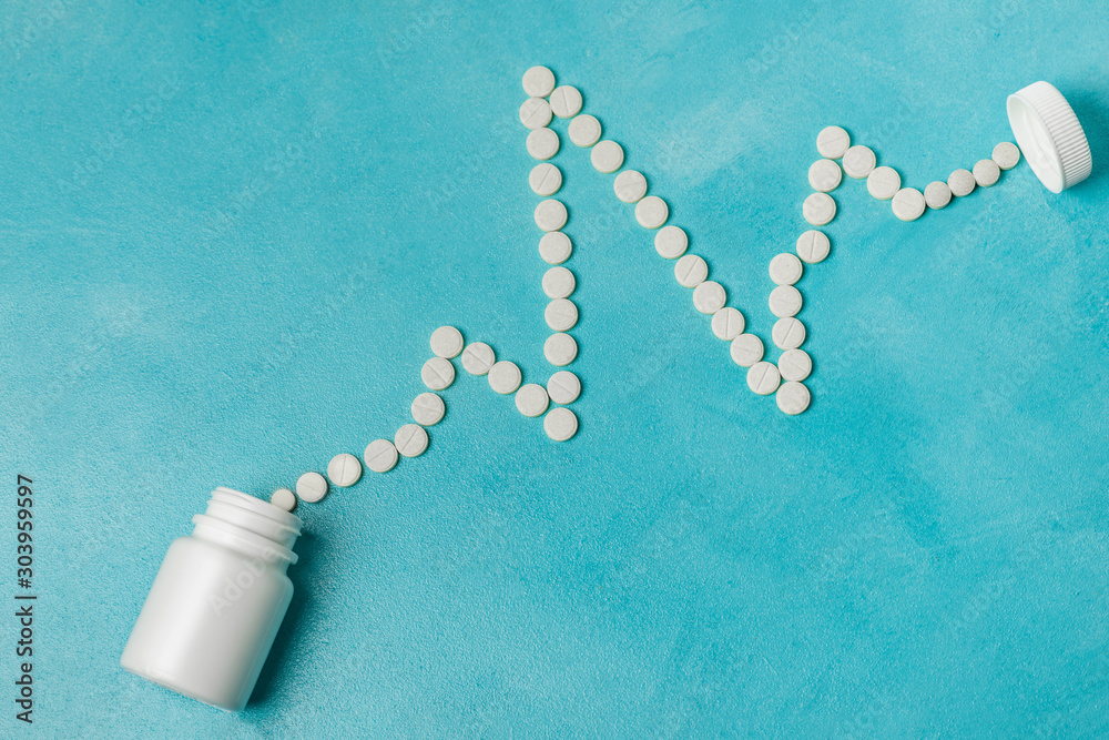 Cardiogram from tablets and white pill bottle on aqua background, copy space