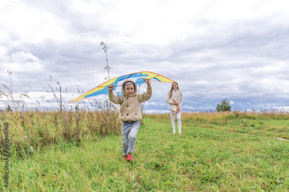 little boy runs along grass, in sweater smiles happy, cheerful and joyful. Launches a kite. Emotions of pleasure and fun. Holiday and birthday concept. In warm clothes on autumn day in nature.