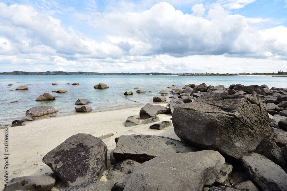 Sandy beach with large stones both on shore and in clear shallow water.