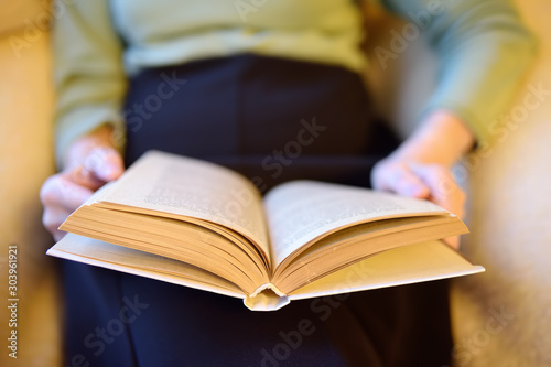 Eldrely woman is reading a book on couch at home.