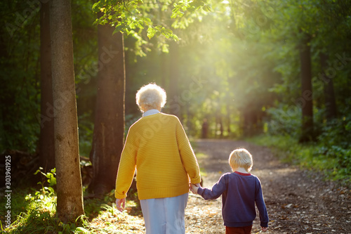 Elderly grandmother and her little grandchild walking together in sunny summer park. Grandma and grandson. photo