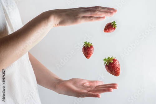 Group of three strawberries hanging in the air between two hands, healthy breakfast