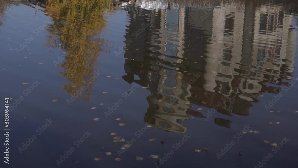 Beautiful huge rural house with brown roof tops and grey walls, located in countryside, is reflected from surface of nearby small pond on clear cold autumn day with blue sky Beautiful huge rural house with brown roof tops and grey walls, located in countryside, is reflected from surface of nearby small pond on clear cold autumn day with blue sky
