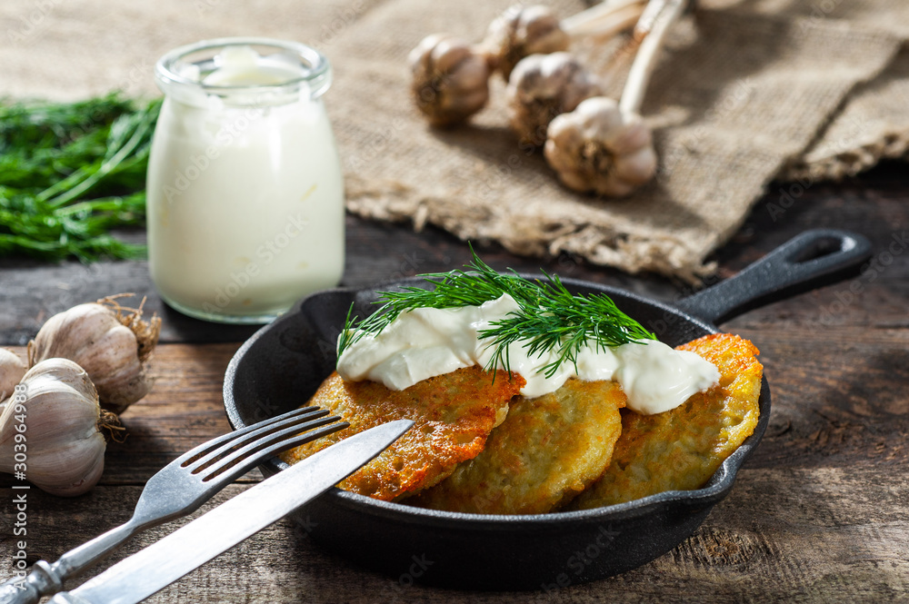 potato pancakes with meat and sour cream lie in a pan seasoned with greens, onions and dill. frying pan with pancakes stands on old wooden background