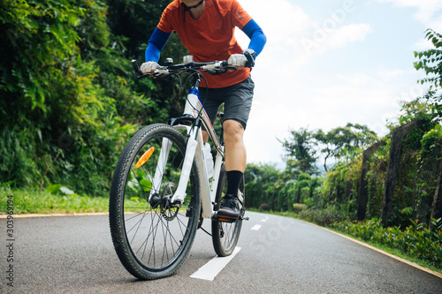 Woman cyclist riding mountain bike on tropical forest trail