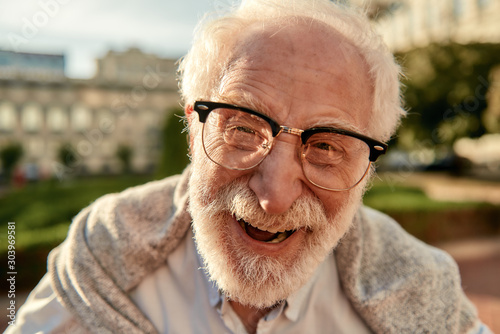 Don’t worry about getting older. Portrait of handsome bearded senior man in glasses looking at camera and smiling while standing outdoors on a sunny day
